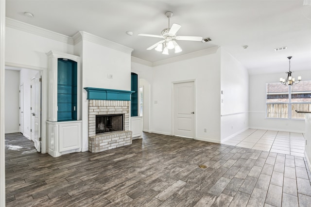 unfurnished living room featuring a brick fireplace, ceiling fan with notable chandelier, dark wood-type flooring, and ornamental molding