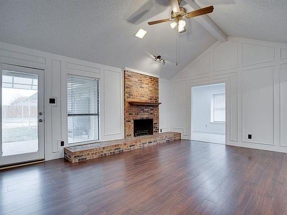 unfurnished living room featuring a brick fireplace, vaulted ceiling with beams, dark hardwood / wood-style floors, and ceiling fan