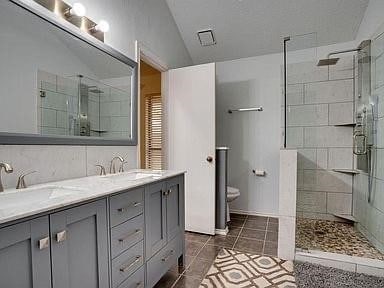 bathroom with vanity, a shower with shower door, tile patterned floors, toilet, and vaulted ceiling