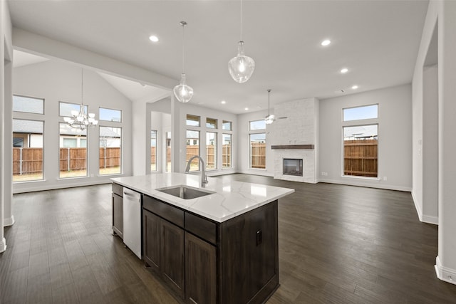 kitchen featuring an island with sink, light stone counters, open floor plan, pendant lighting, and a sink