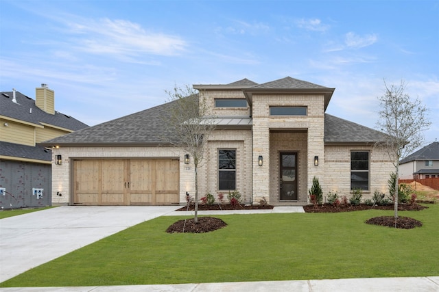 prairie-style house featuring an attached garage, brick siding, a shingled roof, driveway, and a front lawn