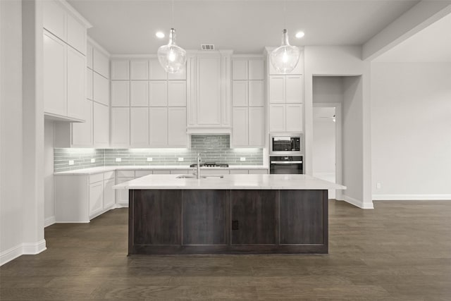 kitchen with an island with sink, decorative light fixtures, built in microwave, white cabinetry, and black oven