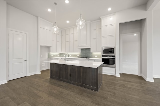 kitchen with pendant lighting, stainless steel appliances, white cabinetry, a sink, and an island with sink