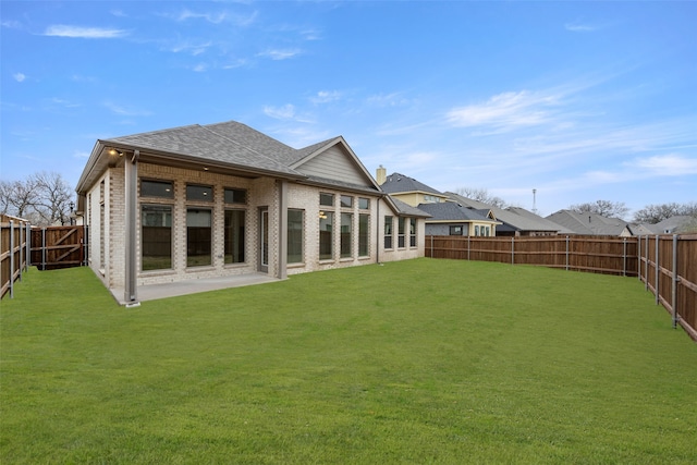 back of house featuring roof with shingles, brick siding, a patio, a lawn, and a fenced backyard