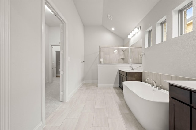 full bath featuring lofted ceiling, two vanities, a shower stall, a freestanding tub, and baseboards