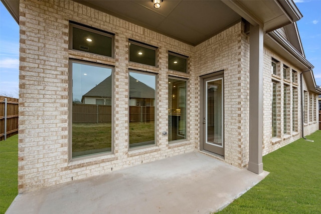 entrance to property featuring brick siding, a yard, fence, and a patio