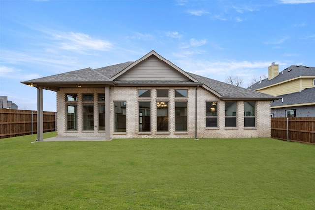 rear view of property featuring a lawn, a patio, a fenced backyard, roof with shingles, and brick siding