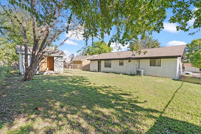 rear view of property featuring a storage unit, central AC unit, and a yard