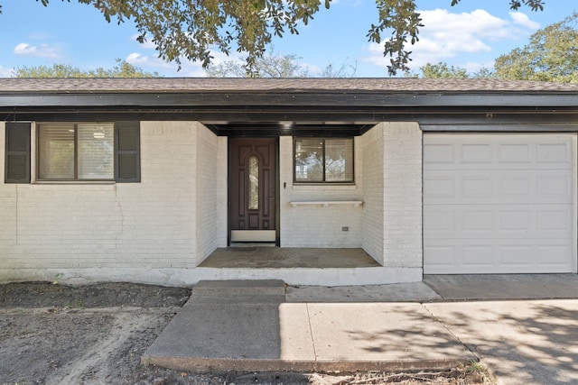 entrance to property with a garage, brick siding, and roof with shingles