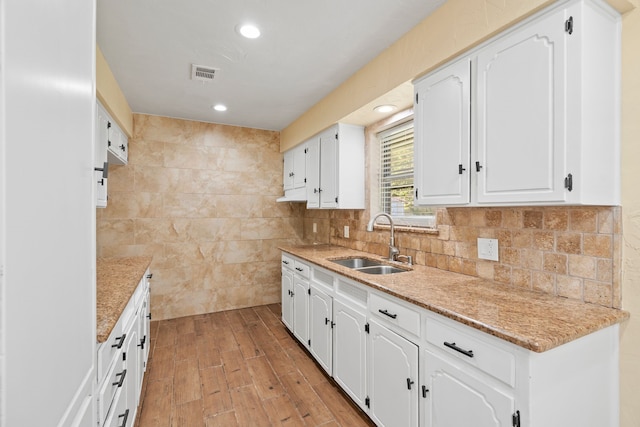 kitchen featuring white cabinets, light stone countertops, sink, and light hardwood / wood-style flooring