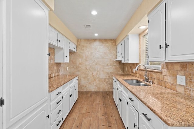 kitchen with white cabinets, light hardwood / wood-style floors, sink, and light stone countertops