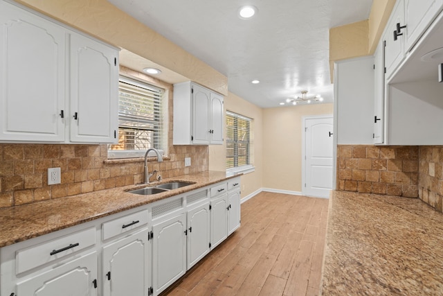 kitchen with white cabinetry, sink, light stone countertops, light hardwood / wood-style flooring, and decorative backsplash