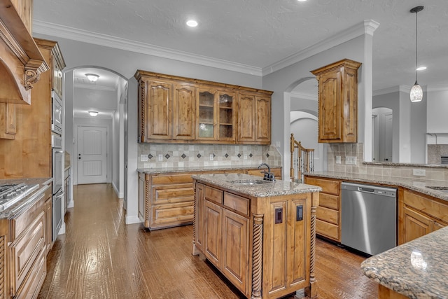 kitchen featuring wood-type flooring, crown molding, appliances with stainless steel finishes, decorative backsplash, and an island with sink