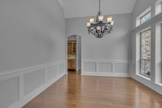 unfurnished room featuring plenty of natural light, wood-type flooring, a chandelier, and vaulted ceiling