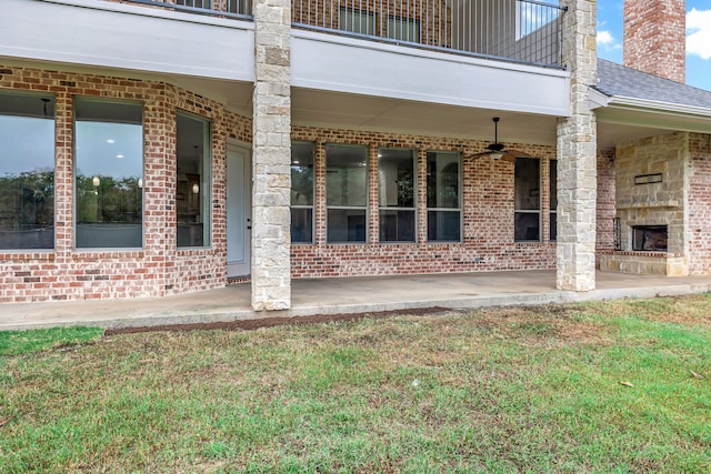 entrance to property with ceiling fan, a balcony, and an outdoor stone fireplace