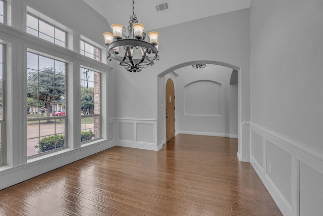 unfurnished dining area featuring a chandelier, vaulted ceiling, and hardwood / wood-style flooring