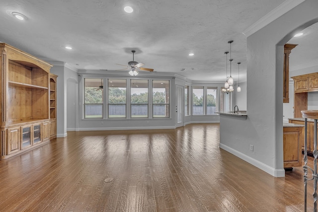 unfurnished living room with crown molding, a textured ceiling, dark hardwood / wood-style flooring, sink, and ceiling fan with notable chandelier