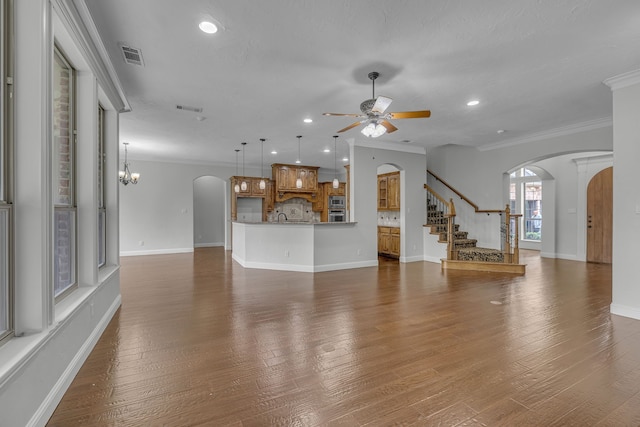 unfurnished living room with ceiling fan with notable chandelier, crown molding, and dark hardwood / wood-style flooring