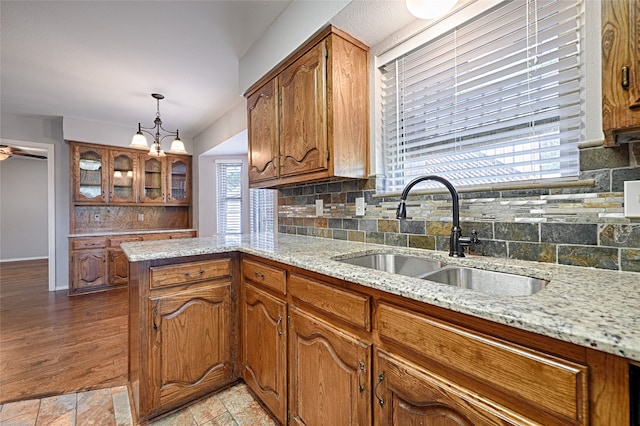 kitchen featuring decorative backsplash, pendant lighting, light stone counters, and sink