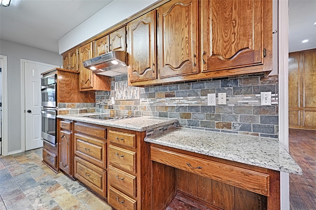 kitchen with light stone countertops, double oven, black electric cooktop, and tasteful backsplash