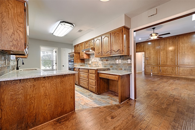 kitchen with decorative backsplash, light stone countertops, kitchen peninsula, and sink