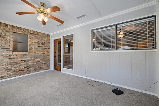 carpeted spare room with ceiling fan, ornamental molding, and brick wall