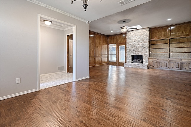 unfurnished living room with a stone fireplace, ceiling fan, ornamental molding, built in features, and light hardwood / wood-style floors