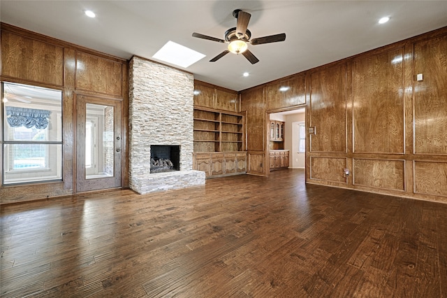 unfurnished living room featuring built in shelves, ceiling fan, a stone fireplace, and dark hardwood / wood-style flooring