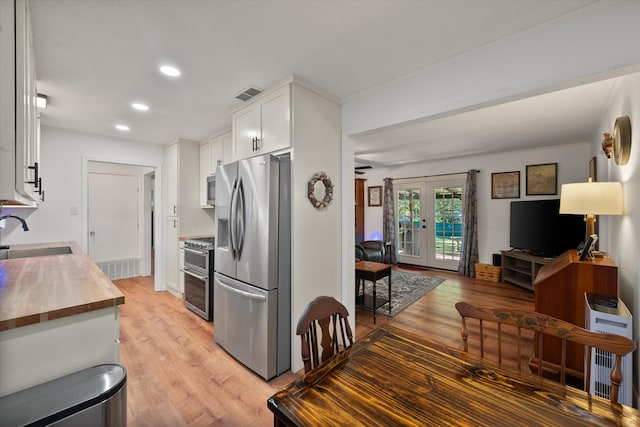 kitchen with wooden counters, white cabinets, sink, light wood-type flooring, and appliances with stainless steel finishes