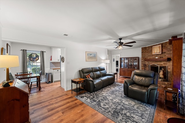 living room with a brick fireplace, ceiling fan, and light wood-type flooring