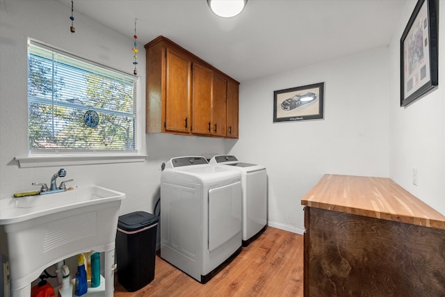 washroom with washing machine and clothes dryer, a wealth of natural light, light hardwood / wood-style flooring, and cabinets