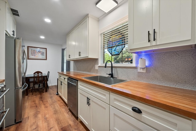 kitchen with butcher block countertops, white cabinetry, sink, and light hardwood / wood-style flooring