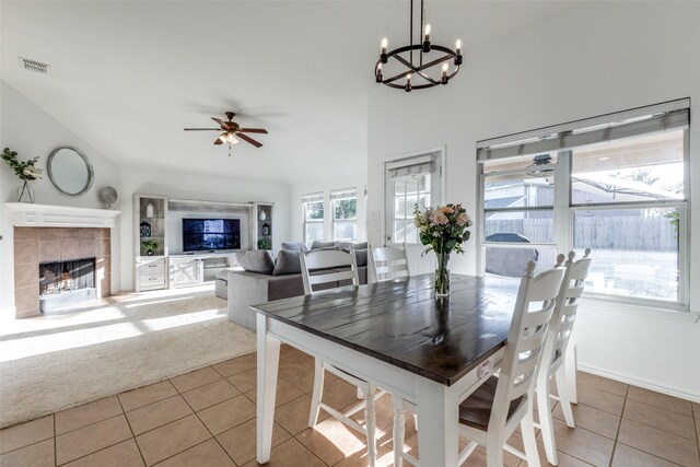 dining area with a fireplace, ceiling fan with notable chandelier, high vaulted ceiling, and light tile patterned flooring