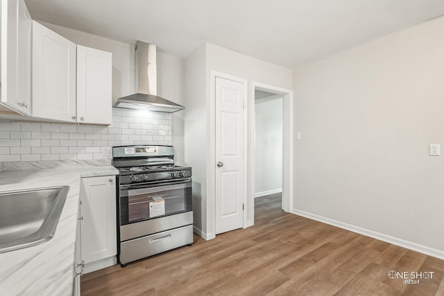 kitchen with white cabinetry, stainless steel range, wall chimney range hood, tasteful backsplash, and light stone counters