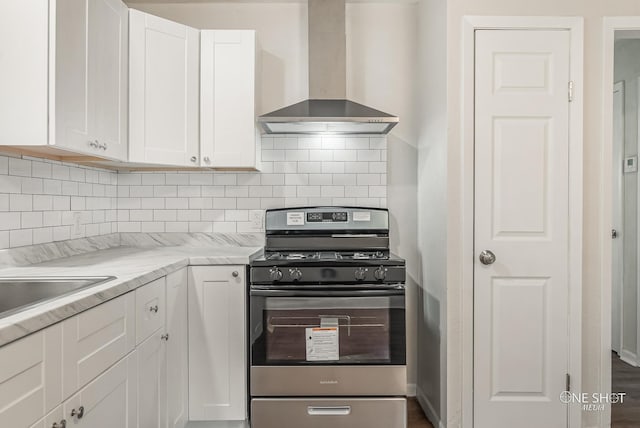 kitchen with stainless steel gas range oven, wall chimney exhaust hood, decorative backsplash, light stone countertops, and white cabinetry