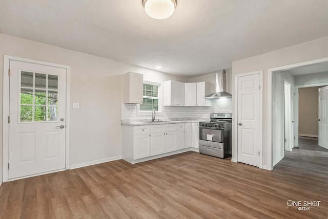 kitchen with backsplash, wall chimney exhaust hood, white cabinets, hardwood / wood-style floors, and stainless steel stove