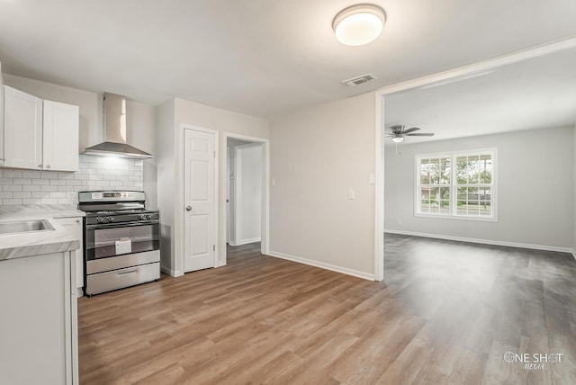 kitchen with stainless steel range, wall chimney range hood, light hardwood / wood-style flooring, backsplash, and white cabinets