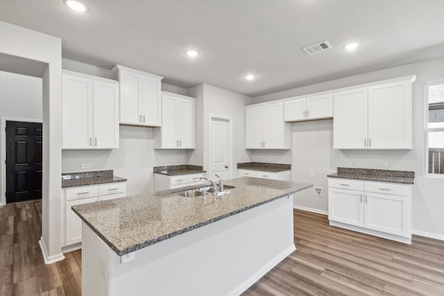 kitchen featuring stone counters, a center island with sink, sink, light wood-type flooring, and white cabinetry