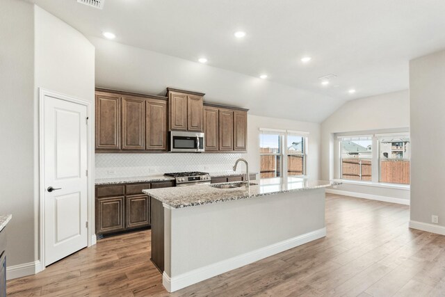 kitchen featuring hardwood / wood-style flooring, stainless steel appliances, a kitchen island with sink, and vaulted ceiling