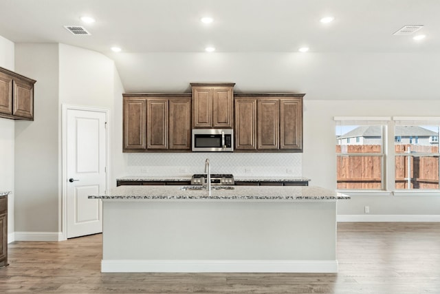 kitchen featuring decorative backsplash, an island with sink, appliances with stainless steel finishes, light hardwood / wood-style floors, and light stone counters