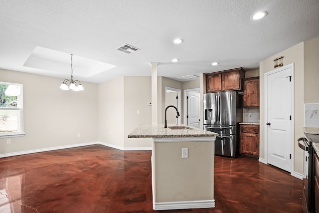 kitchen with light stone counters, stainless steel fridge, sink, a chandelier, and a kitchen island with sink