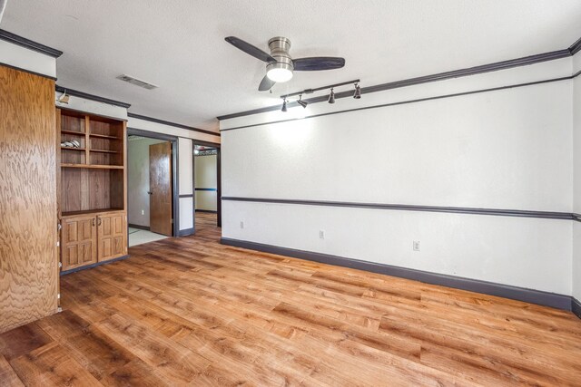 empty room with a textured ceiling, ornamental molding, wood-type flooring, and ceiling fan