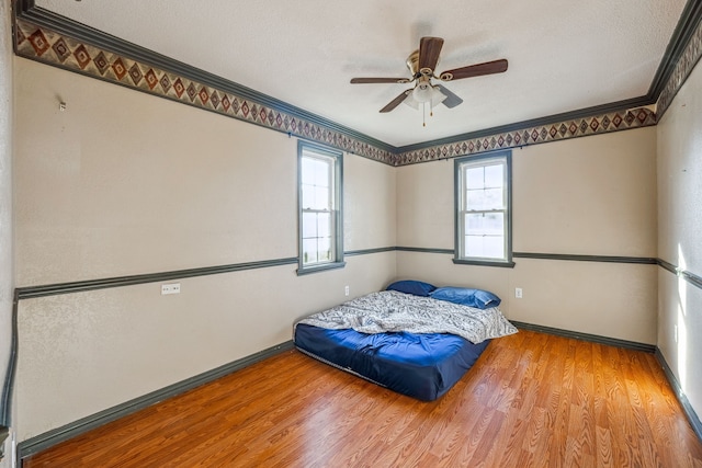 bedroom featuring a textured ceiling, wood-type flooring, ceiling fan, and crown molding