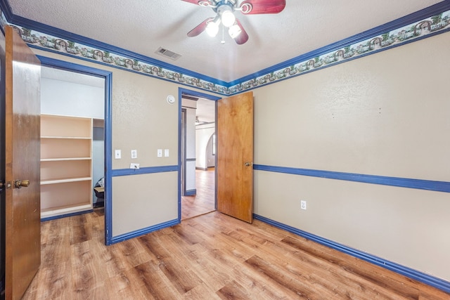 unfurnished bedroom featuring ceiling fan, a textured ceiling, hardwood / wood-style floors, crown molding, and a closet