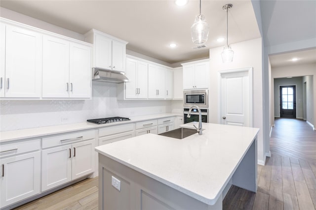 kitchen featuring stainless steel appliances, light wood-type flooring, decorative light fixtures, white cabinets, and a kitchen island with sink