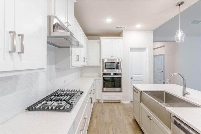 kitchen featuring light wood-type flooring, appliances with stainless steel finishes, pendant lighting, decorative backsplash, and white cabinets