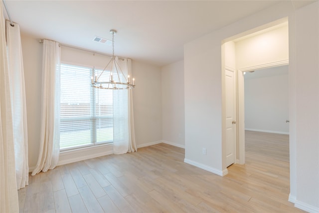 empty room with a chandelier, a wealth of natural light, and light hardwood / wood-style floors