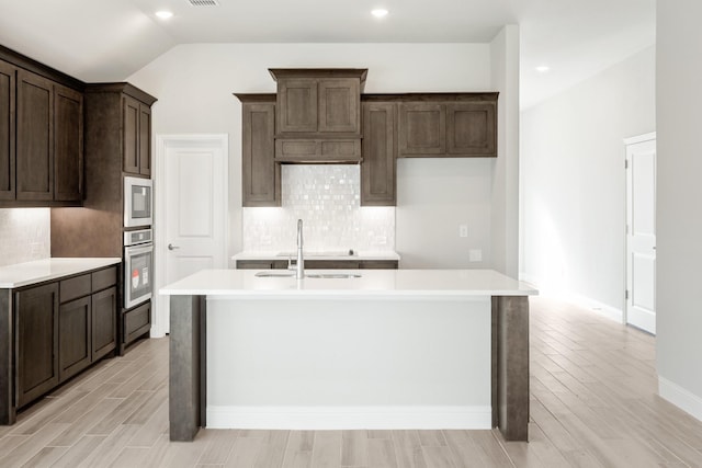 kitchen with lofted ceiling, sink, decorative backsplash, a kitchen island with sink, and stainless steel oven