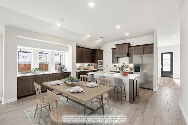 kitchen with dark brown cabinetry, sink, appliances with stainless steel finishes, an island with sink, and light hardwood / wood-style floors