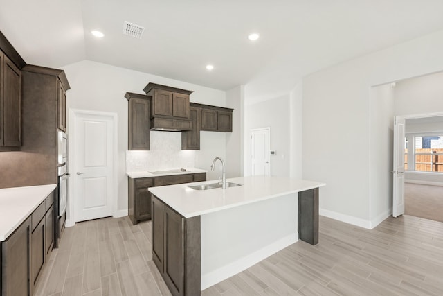 kitchen featuring sink, tasteful backsplash, vaulted ceiling, black electric cooktop, and an island with sink